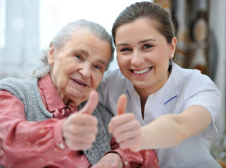 aide and elderly woman doing a thumbs up